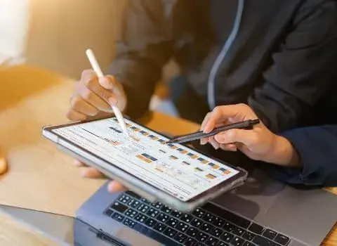 Two people reviewing cost analysis on a tablet with charts, representinghidden fees in card payment processing.